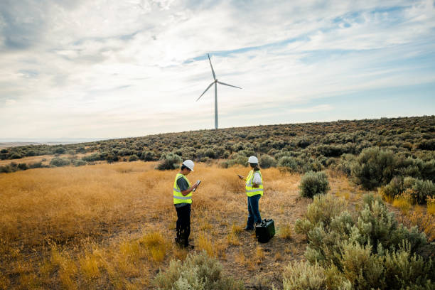 Technicians Working On Wind Farm With Turbines In Background