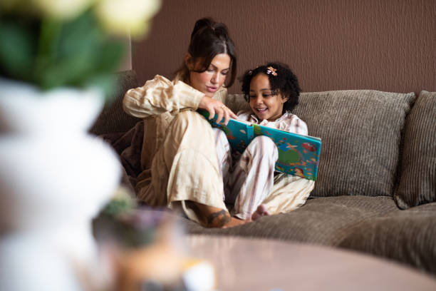 Relaxed mother and daughter reading a book on sofa.