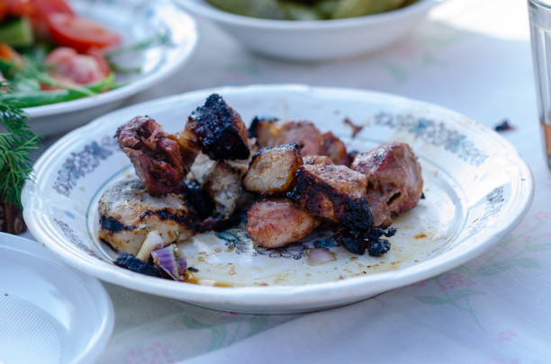 A half-empty plate with leftovers of grilled pork meat, with some charred pieces.