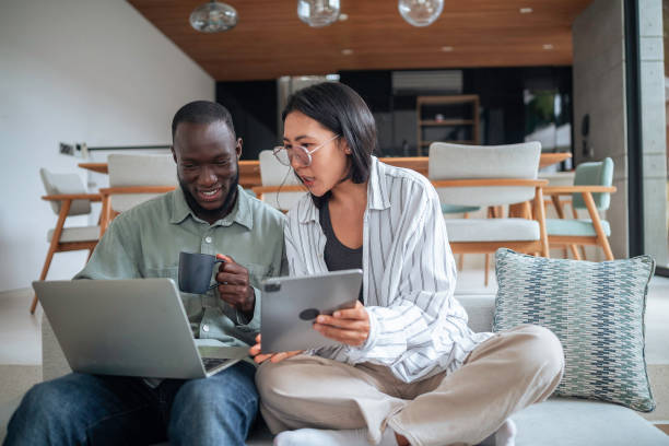 istock Asian Woman and Black Man with Tech Gadgets on Sofa 2168120289
