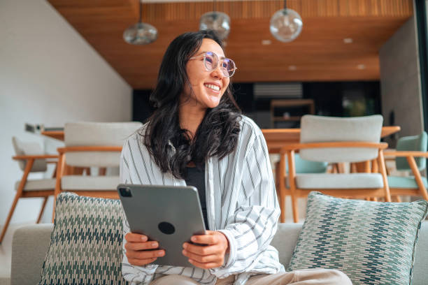 istock Smiling Asian Woman Engaging with Tablet on Home Sofa 2168120348