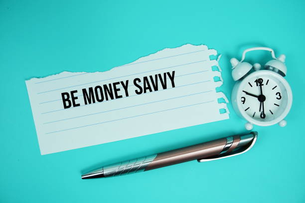 istock Be Money Savvy text written on paper torn with alarm clock top view on blue background 2168145092