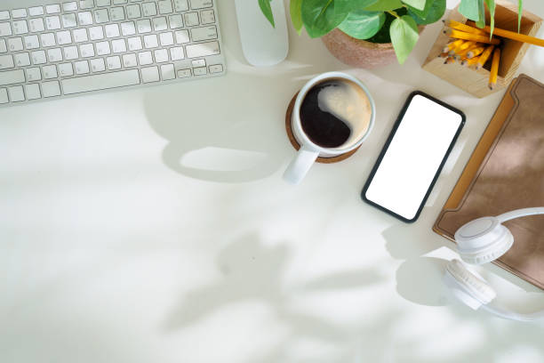 istock Smart phone with blank screen, notebook and cup of coffee on white office desk. Flat lay, Top view. 2168150007
