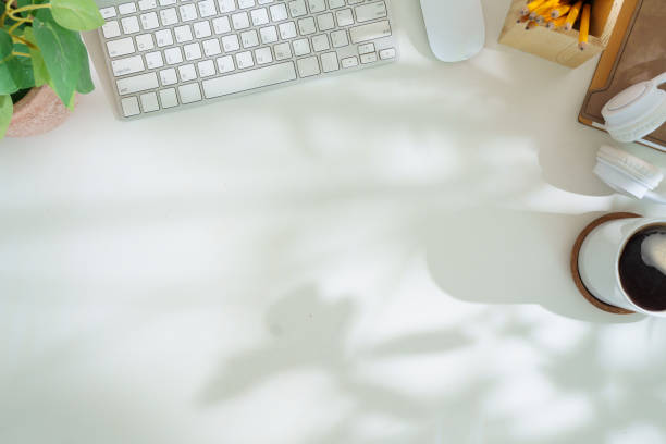 Top view white office desk with keyboard, coffee cup, headphone and stationery.