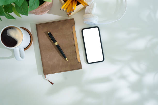 istock Smart phone with blank screen, notebook and cup of coffee on white office desk. Flat lay, Top view. 2168150011