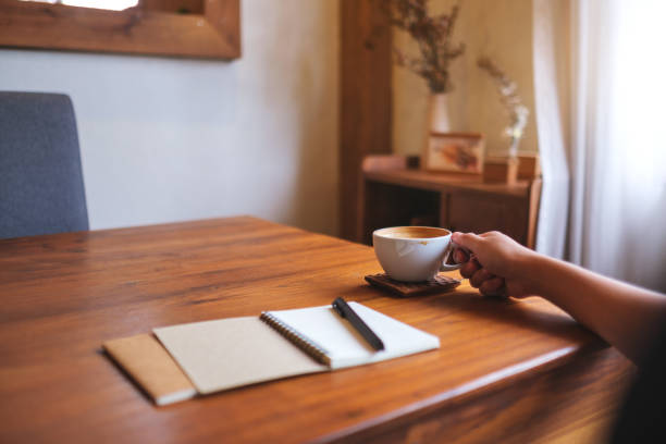istock Closeup image of a woman drinking coffee with a blank notebook on the table 2168155740