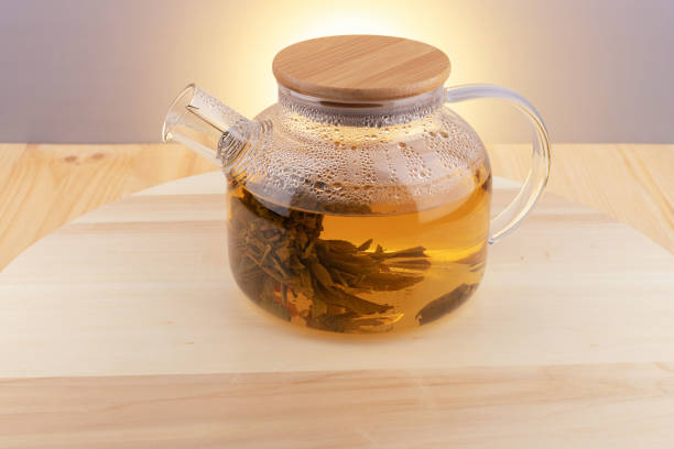 Large leaf tea is brewed in a glass teapot, which is on a round wooden tray on the table.