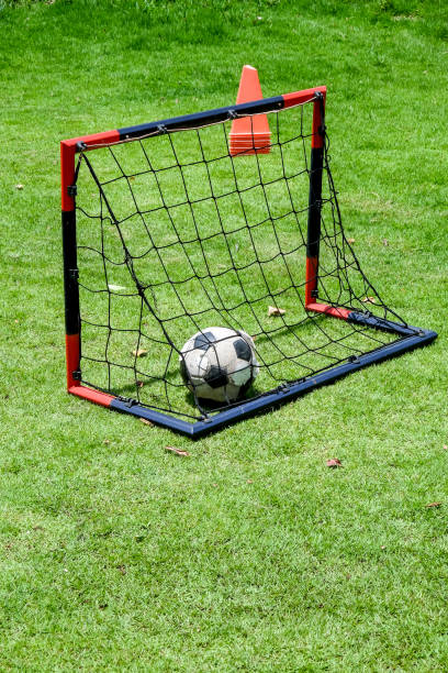 istock Soccer ball in goal net on green grass field with red cones 2168160721