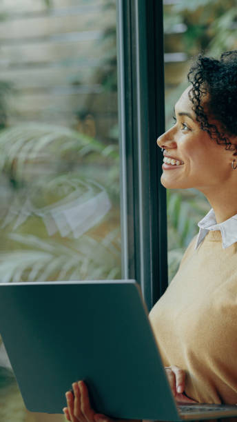 istock A cheerful woman works diligently on her laptop by a window surrounded by greenery 2168164096