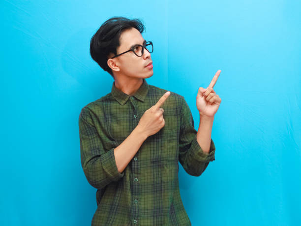 istock Serious-looking concerned asian male poses pointing to copy space standing blue backgrou 2168178107