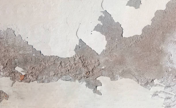 istock Weathered Wall Texture with Peeling Paint revealing the underlying concrete or plaster. The surface is uneven and shows signs of wear and tear, with cracks, chips, and exposed patches 2168185682