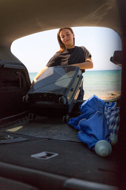 istock Young woman placing black suitcase in the trunk 2168187627