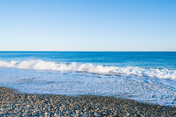 istock Crystal Blue Waves Gently Embrace the Pebbled Shore 2168195009