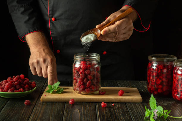 istock Adding sugar with a spoon to a jar of raspberries before canning on the kitchen counter. The concept of making raspberry jam by hand of a chef 2168202664