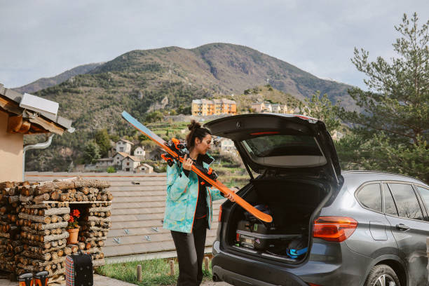 Two middle-aged women arriving at a rustic cabin on a sunny winter day, unloading colorful suitcases from a blue SUV to begin a peaceful countryside weekend retreat