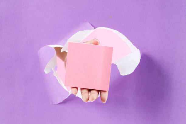 istock Pink Sticky Notes Holding by Female Hand on Paper RIp Hole Purple Background 2168209072