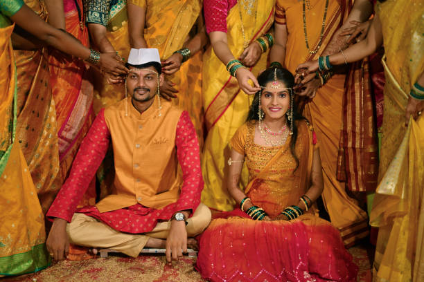 Bride and Groom with Mundawali (sacred thread) on their foreheads during their haldi ceremony This image capturing the bride and groom together during the Haldi ceremony, both adorned with the Mundawali, a sacred thread tied across their foreheads. The couple, dressed in traditional yellow attire, sit side by side, with warm smile and the women around them touching the thread. The Mundawali symbolizes protection and blessings as they prepare for their upcoming wedding haldi ceremony stock pictures, royalty-free photos & images