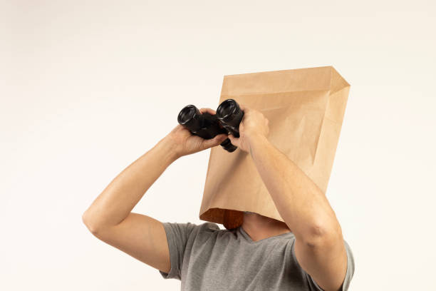 Man wearing paper bag looks through binoculars.