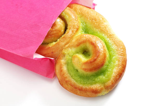 Bun with pistachio cream in pink paper bag on an a white background close-up