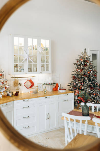 Cozy Christmas kitchen reflection in a mirror, showcasing a frosted tree with red ornaments, white cabinets, and festive holiday decorations for a warm, inviting ambiance