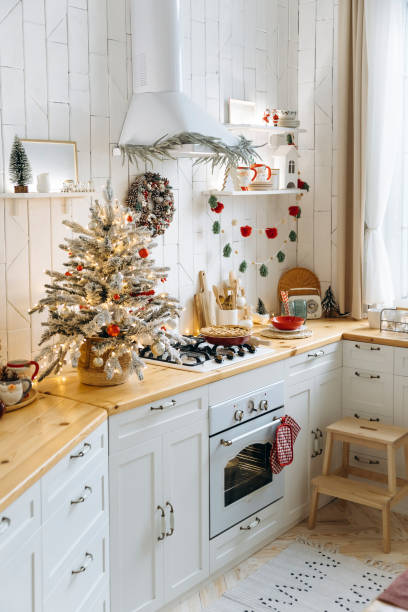 istock Holiday kitchen decor with a Christmas tree on the counter, pinecone wreath, and festive garland. Wooden countertops, white cabinets, pie on the stove, warm holiday feel 2168224381