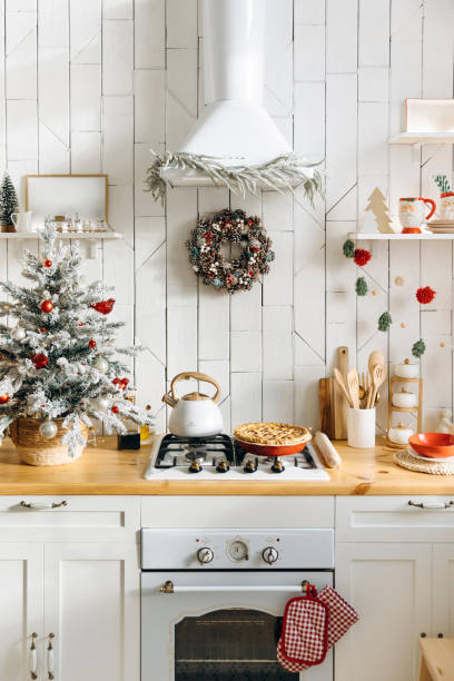 istock Cozy kitchen decorated for Christmas featuring a frosted mini tree with red and silver ornaments, a pinecone wreath above the stove, and a freshly baked pie on the counter 2168224690