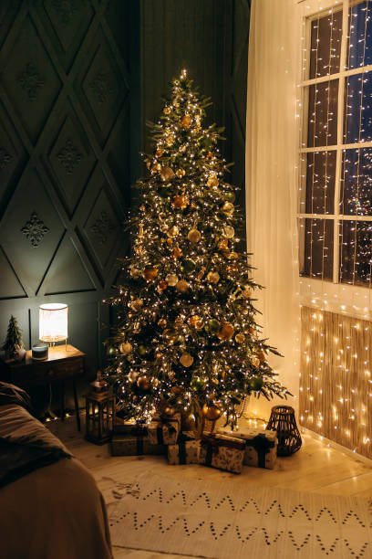 istock Christmas tree with Christmas decorations and gift boxes on the floor, shining with many lights from a garland in a cozy bedroom. Christmas Eve Magic. Cozy Christmas at home. New year's night 2168225144