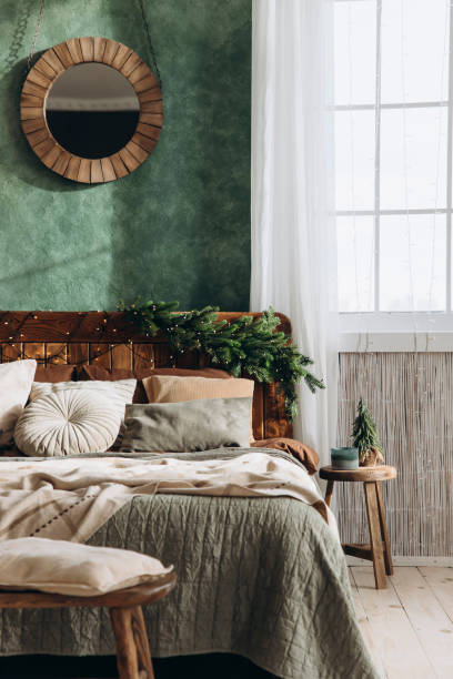 istock Large wooden double bed with festive decorations, green wall, and round mirror situated by a window letting in natural light. Cozy, airy atmosphere 2168225418