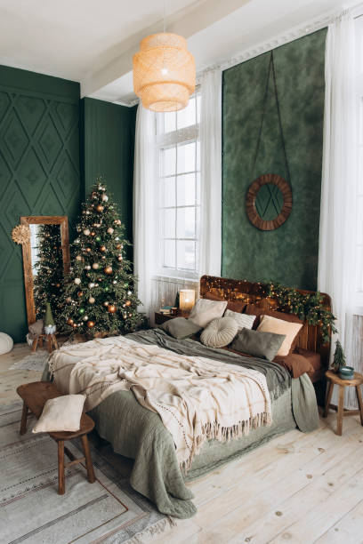 istock Elegant bedroom with Christmas decor, featuring large tree, cozy bed with pillows and blankets, wooden dresser, full-length mirror, and large windows. Green walls enhance festive atmosphere 2168225707