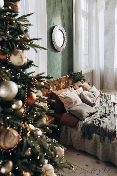 istock View through a Christmas tree at a large double bed with wooden headboard in a spacious bedroom with green walls and large windows, filled with sunlight. Cozy and festive atmosphere 2168226597