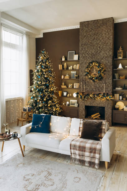istock Stylish holiday living room with a decorated Christmas tree, a white sofa with string lights, a stone fireplace with a wreath, bookshelves, and large windows with sheer curtains 2168226823