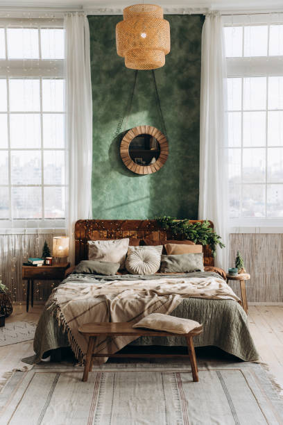 istock Double bed with wooden headboard placed between two large windows in spacious Christmas-decorated bedroom. Sunlight fills the room, highlighting green walls and festive decor 2168227052