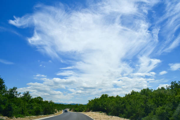istock Big white cloud dominating blue sky, car on road 2168247377