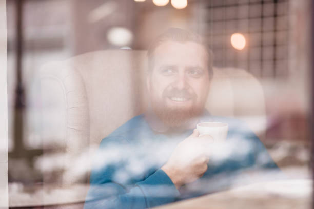 A man enjoys his coffee through a window, capturing a cozy evening atmosphere in a cafe.