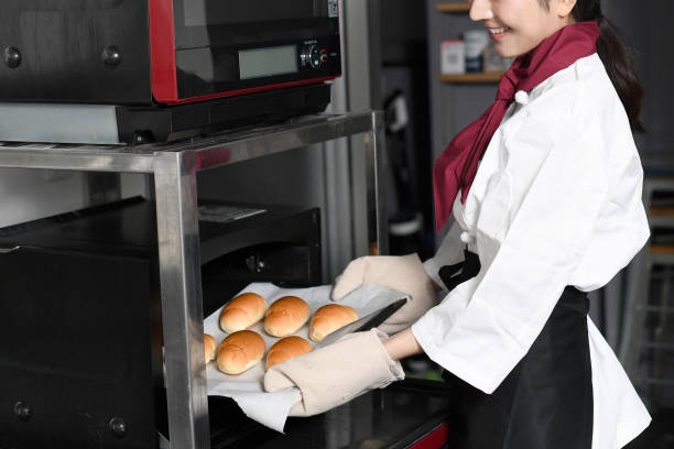 Young baker woman making bread in the oven in the kitchen