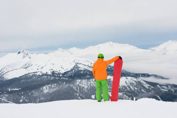 Snowboarder stands on mountain above valley, Whistler, B.C.
