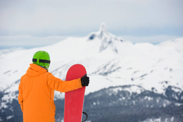 Snowboarder stands on mountain above valley, Whistler, B.C.