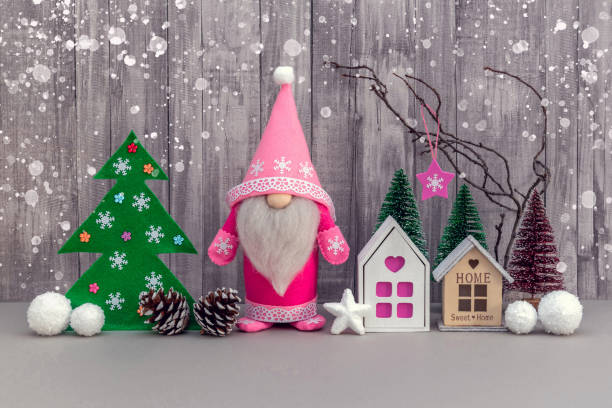 A handmade pink felt Christmas gnome, pine cones and a mock-up of the house are decorated with snowflakes. Christmas and New Year decorations on a gray background.