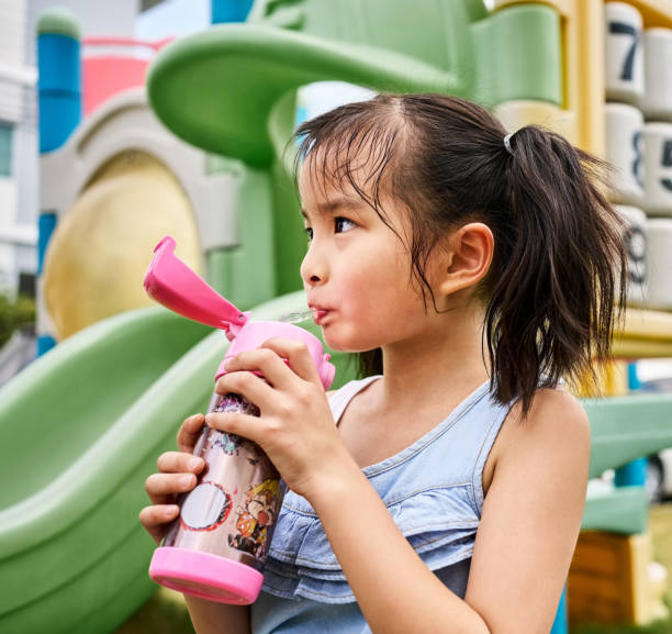 Cute little girl drinking from a water bottle after an active session at the children playground
