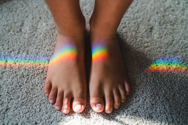Close-up of two bare feet with vibrant rainbow reflections on a soft carpeted surface, highlighting light dispersion through a glass prism