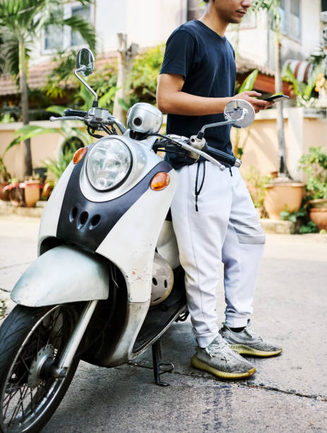 istock Young man standing by his moped and using mobile phone outside 2168277414