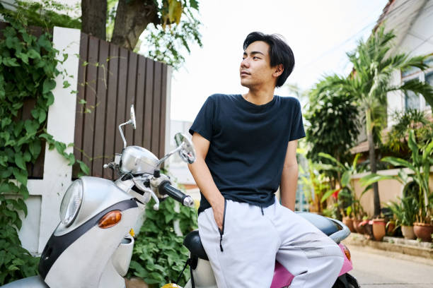 Handsome young asian man sitting on his scooter and looking away on the street outside
