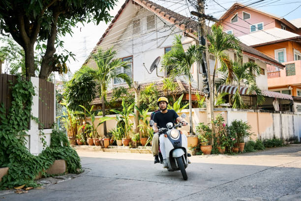 Motorcycle taxi driver carrying a young male customer during the morning hours along a side street