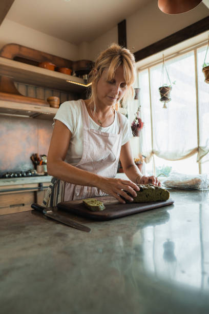 Baker woman slicing loaf of bread on wooden cutting board