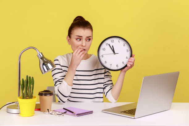 istock Unhappy woman office worker biting finger nails, holding wall clock talking video call on laptop. 2168287733