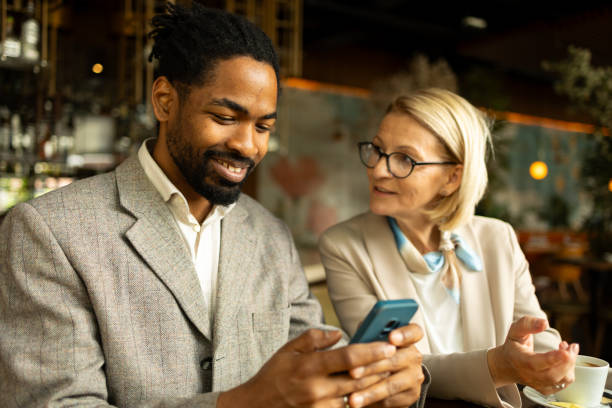 istock Two smiling colleagues in a cozy cafe discussing work while looking at a smartphone. The relaxed atmosphere and friendly interaction suggest a positive and collaborative professional environment. 2168288002