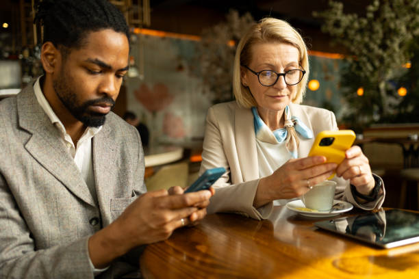 istock Two business professionals are focused on their smartphones while sitting at a modern cafe table. The image portrays a serious work environment amidst a casual setting, showcasing the integration of technology in daily business operations. 2168288008