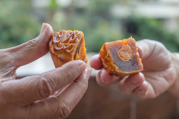 Close-up shot of Unrecognizable couple Eating Mooncake Chinese pastry. Both of hands holding a quarter cut of the mooncake slices.