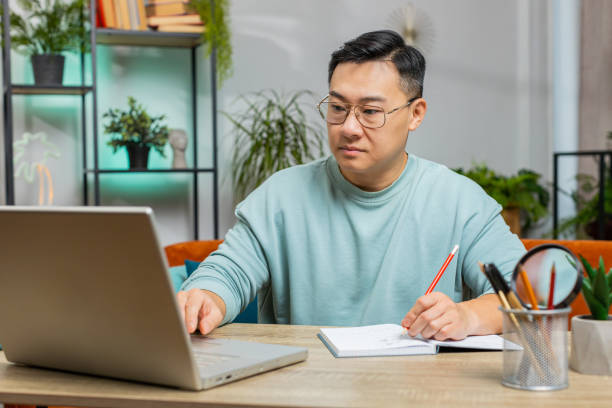 istock Asian man freelancer making notes on notebook at home, use laptop, prepare business financial report 2168290884