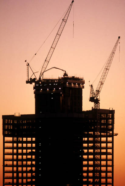 Exterior distant view of industrial cranes on a building construction site silhouetted against a spectacular sunset sky